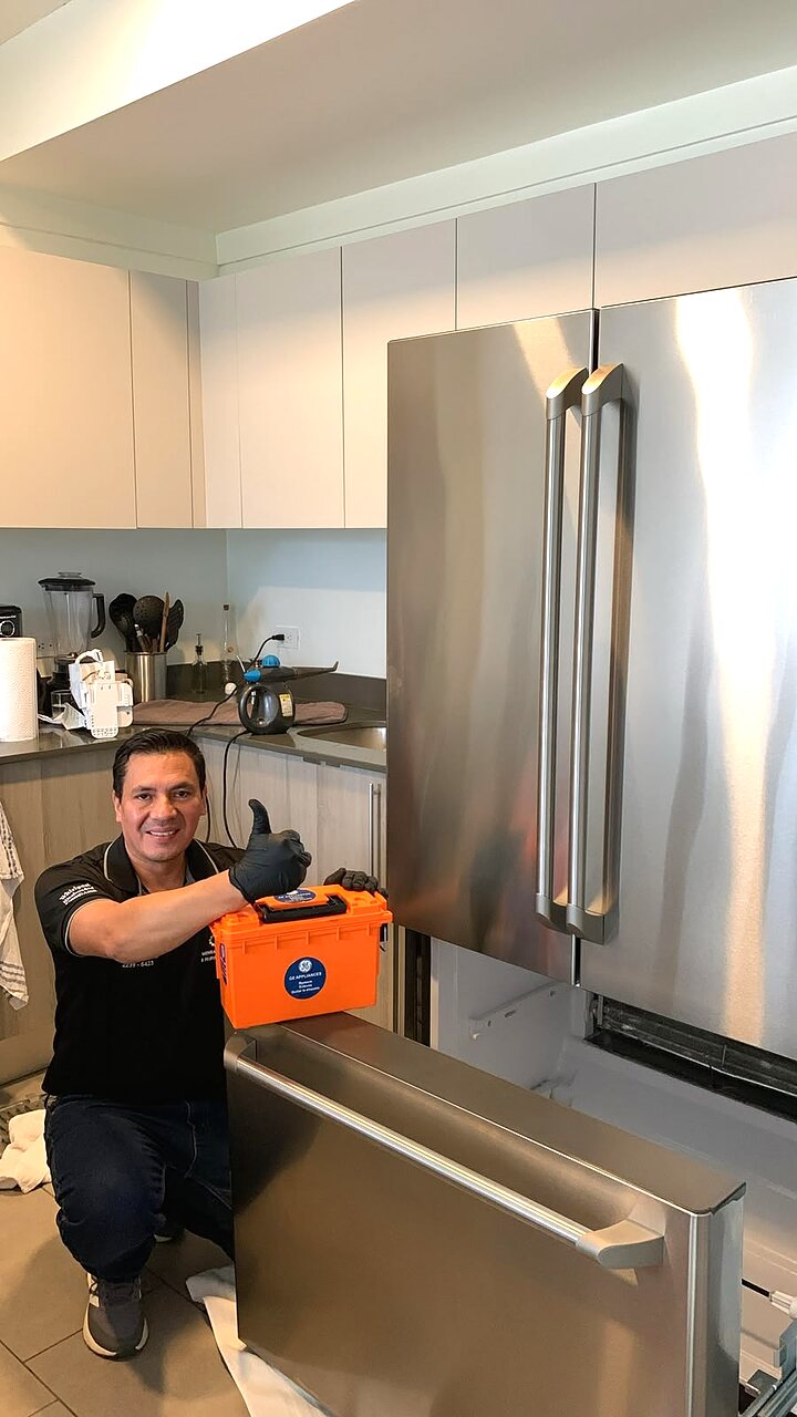 Técnico Mengar con caja de repuestos originales GE junto a refrigeradora French Door